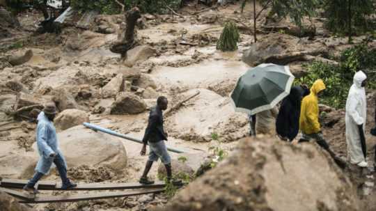 Ľudia kráčajú cez rozvodnenú rieku po vyčíňaní cyklóny Freddy v meste Blantyre v Malawi.