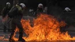 Príslušníci gréckych poriadkových síl kráčajú cez plamene horiacich petrolejových bômb, ktoré hádzali demonštranti počas zrážok v centrálnych Aténach.
