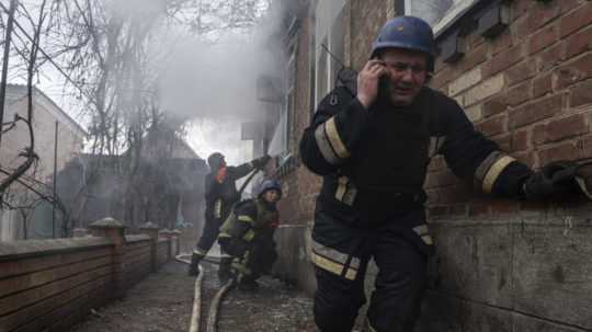 Záchranár telefonuje a jeho tím hasí požiar v dome, ktorý ostreľovali ruské sily v obytnej štvrti mesta Kosťantynivka v Doneckej oblasti na východe Ukrajiny v piatok 10. marca 2023.