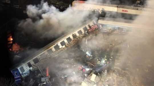 Dym stúpa z vlakov, zatiaľ čo hasiči a záchranári pracujú po zrážke pri meste Larisa v Grécku.