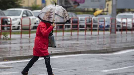 Na snímke žena s dáždnikom prechádza cez cestu v centre Bratislavy počas silného dažďa.