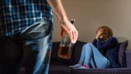 Na snímke sa žena bráni pred mužom držiacim sklenú fľašu alkoholu.