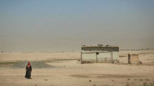 Dom na púšti, pred ktorým stojí zahalená postava.