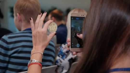 Na snímke žena drží telefón a mincu s logom kryptomeny.