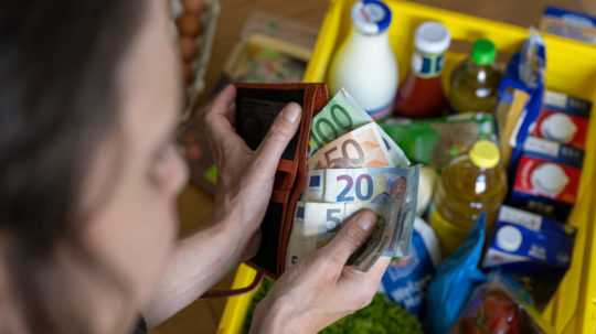 Žena si dáva do peňaženky eurové bankovky nad košom s nákupom.