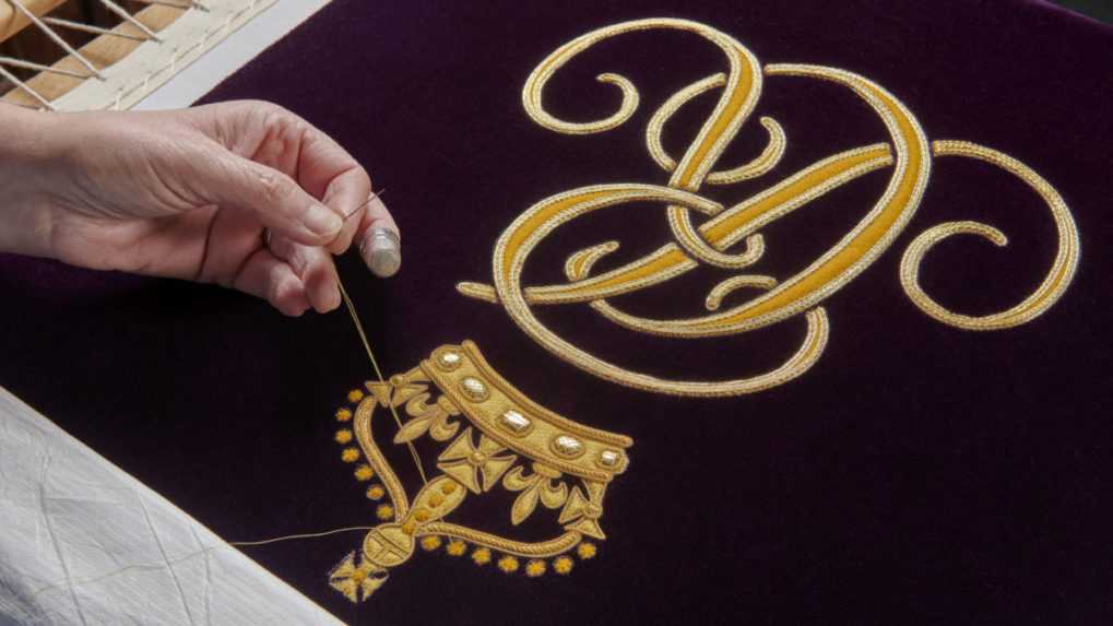 Vyšívanie monogramu na purpurovej korunovačnej róbe, ktorú bude mať na sebe oblečenú Kamila počas korunovácie pri odchode z Westminsterského opátstva.