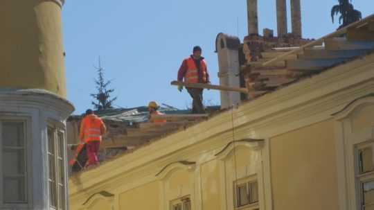 na snímke robotníci na streche budovy.