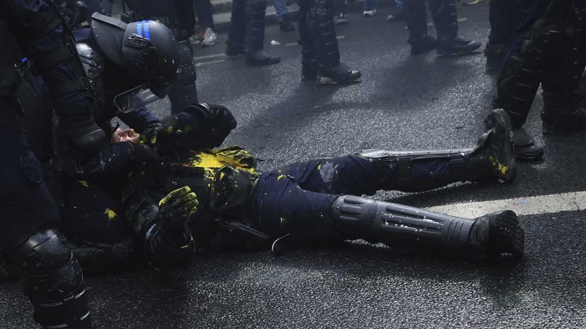 Na snímke príslušník poriadkovej polície leží na chodníku počas demonštrácie v pondelok 1. mája 2023 v Paríži.