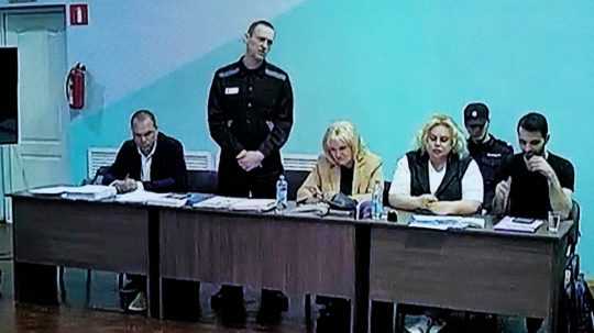 Pohľad na televíznu obrazovku, na ktorej ruský opozičný líder Alexej Navaľnyj (druhý zľava) stojí medzi svojimi právnikmi v súdnej sieni.