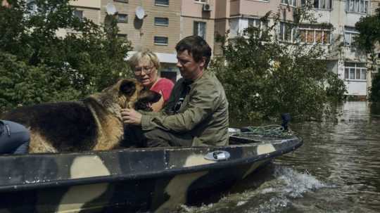 Miestni obyvatelia a ich pes sedia v člne počas evakuácie zo zaplavenej štvrti v ukrajinskom meste Cherson vo štvrtok 8. júna 2023.