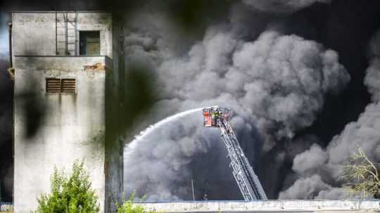 Požiarnici na rebríku hasia vodou oheň, ktorý vypukol v hale na výrobu plastov.