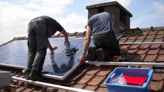 Na snímke muži montujú na strechu solárne panely.
