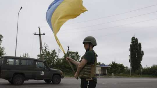 Chlapec máva ukrajinskou vlajkou neďaleko diaľnice v meste Lyman.