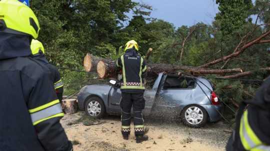 Na ilustračnej snímke hasiči odstraňujú polámané konáre stromu z osobného auta po silnej búrke v Záhrebe v stredu 19. júla 2023.
