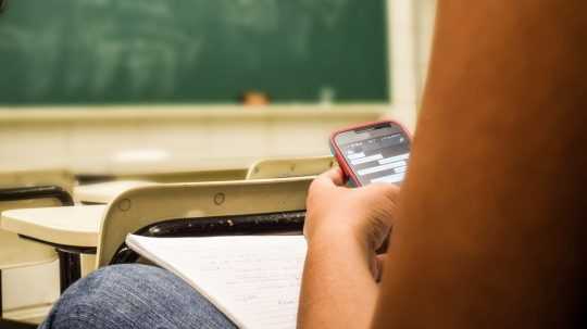 Na snímke žiak drží smartfón v lavici v triede.