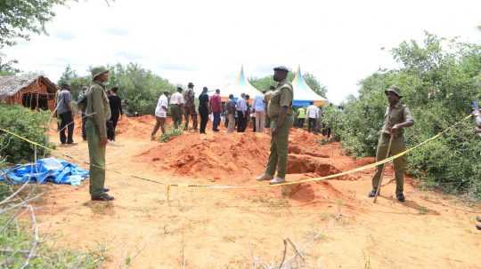 Policajti vykopávajú telá z hromadného hrobu.