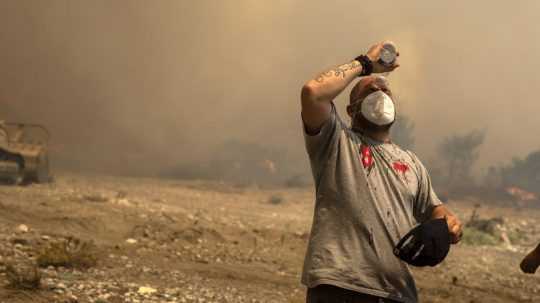 Dobrovoľník sa polieva vodou počas hasenia lesného požiaru v obci Vati na ostrove Rodos.