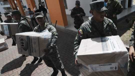 Na sníme ekvádorskí vojaci nesú krabice s materiálom do volebnej miestnosti.