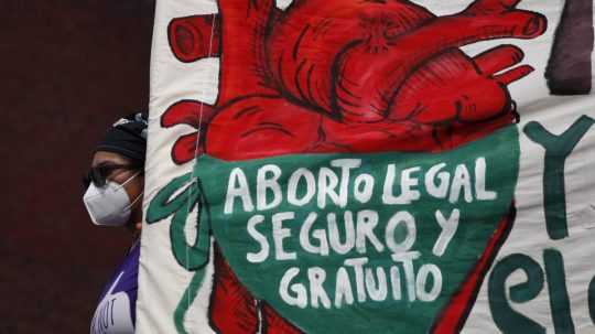 Žena drží transparent s nápisom v španielčine: "Legálne, bezpečné a bezplatné potraty".