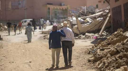 Ľudia kráčajú okolo trosiek zničených budov po zemetrasení v Amizmize.