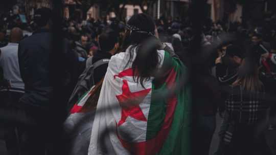 Na snímke žena s vlajkou Alžírska uprostred davu.