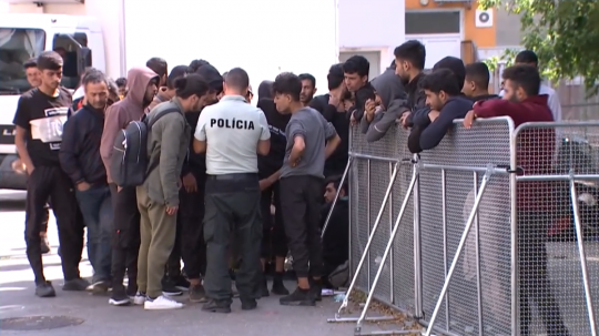 Skupina migrantov pri príslušníkovi polície.
