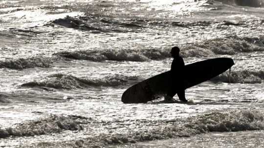 Muž nesie surf na jednej z pláží vo Walese.