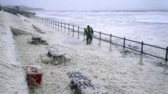 Muž kráča cez morskú penu v Seaburne na severovýchode Anglicka.