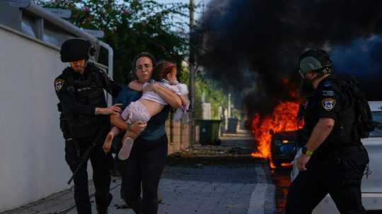 policajt pomáha žene s dieťaťom v náručí pri evakuácii z miesta, ktoré zasiahla raketa