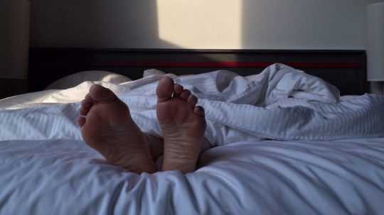 Osoba leží v posteli prikrytá paplónom, spod ktorého jej trčia chodidlá.