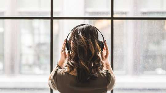 Žena počúva hudbu zo slúchadiel hľadiac cez okno.