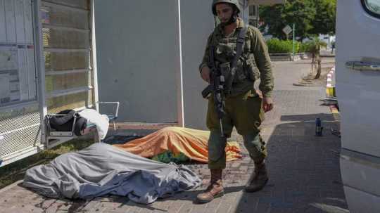 Izraelský vojak stojí pri telách Izraelčanov zabitých po palestínskom raketovom útoku z pásma Gazy.
