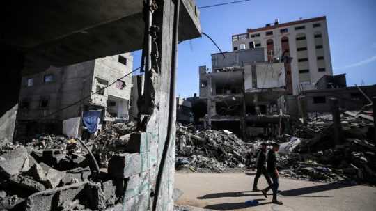 Palestínčania kráčajú medzi troskami zničených budov v centrálnom pásme Gazy.