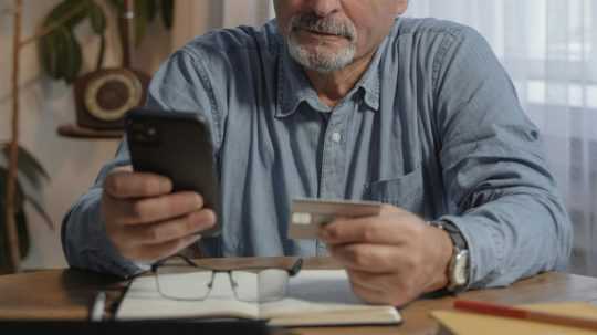 Muž na snímke nakupuje online pomocou telefónu, drží platobnú kartu.