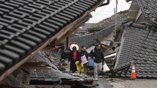 Ľudia kráčajú cez spadnuté budovy po zemetrasení v meste Suzu.