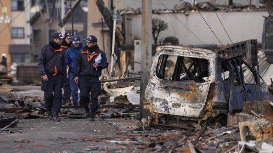 Japonskí hasiči prechádzajú okolo vrakov zhorených áut po požiari po zemetrasení.