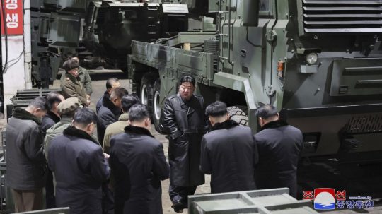 Severokórejský vodca Kim Čong-un (uprostred) v koženej čiernej bunde počúva počas návštevy továrne na výrobu zbraní.