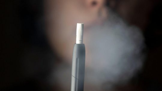 Na snímke žena v oblaku dymu, v popredí elektronická cigareta.