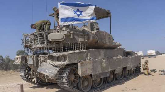 Izraelský vojak pripevňuje izraelskú vlajku na obrnený transportér.