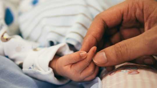 Na snímke ženská ruka drží ruku novorodenca.