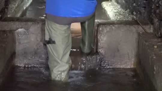 Pracovník sa brodí vodou v podzemnej chodbe.