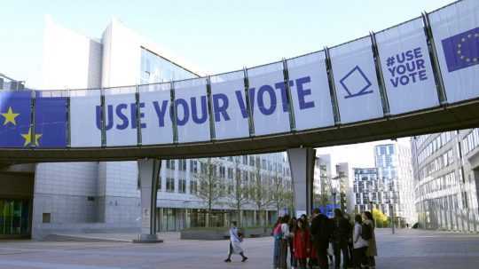 Ľudia stoja pod volebným transparentom pred Európskym parlamentom v Bruseli.