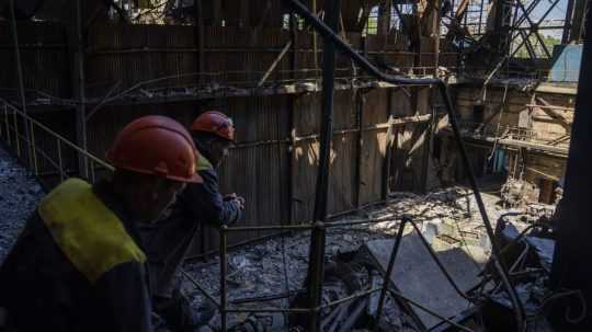Pracovníci stoja vedľa trosiek v poškodenej tepelnej elektrárni DTEK.