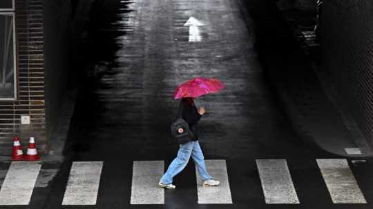 Žena s dáždnikom prechádza cez cestu.