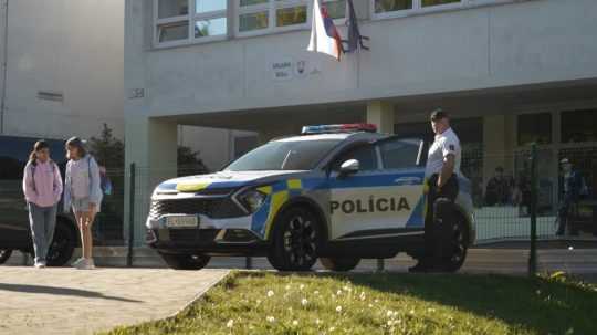 Policajt stojí pred budovou základnej školy.