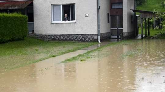 Muž pozerá z okna domu na zaplavený dvor v obci Kamenná Poruba.