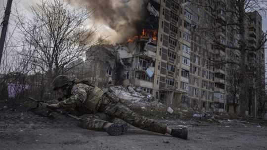 Ukrajinský policajt sa kryje pred horiacou budovou, ktorá bola zasiahnutá pri ruskom leteckom útoku v Avdijivke.