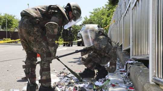 Juhokórejskí vojaci v ochrannom oblečení kontrolujú odpadky z balónov.