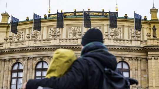 Ilustračná snímka - dvaja ľudia sa objímajú pri pohľade na čierne zástavy vejúce na budove Karlovej univerzity v Prahe.