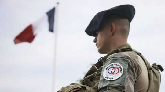 Vojak stojí pri francúzskej vlajke.